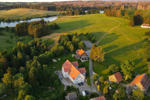 Vista aérea de una tiny house en Alemania rodeada de campos verdes, árboles y un lago tranquilo en el campo.