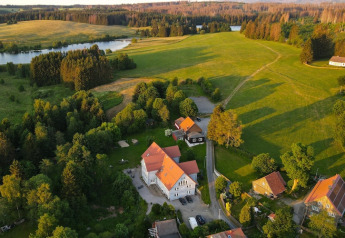 Vue aérienne d'une tiny house en Allemagne entourée de champs verts, d'arbres et d’un lac paisible à la campagne.