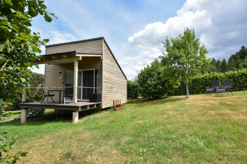 Casa mobile Holiday home Terra 2 Persons con veranda in legno, prato verde, alberi e sedie all’aperto.