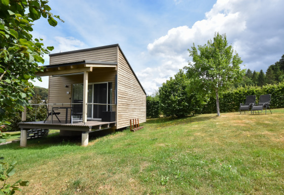 Mobilhome Holiday home Terra 2 Persons met houten terras, grasplein en tuinstoelen in een groene omgeving.