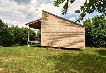 Modern mobile home 'Terra 2 Persons' in Germany, wood siding and covered terrace in a green natural setting.