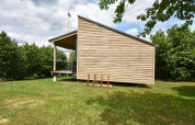 Mobil-home moderne « Terra 2 Persons » en Allemagne, revêtement bois et terrasse couverte dans un cadre vert.