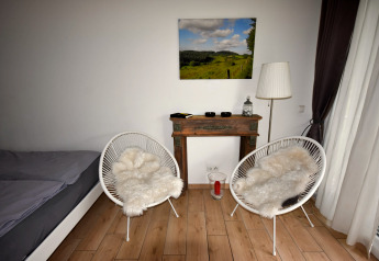 Moderne mobilhome med to stole, pelsbetræk, et lille bord, seng og landskabsbillede på væggen.