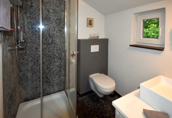 Salle de bains moderne dans mobil-home avec douche, WC suspendu, petite fenêtre et lavabo blanc.
