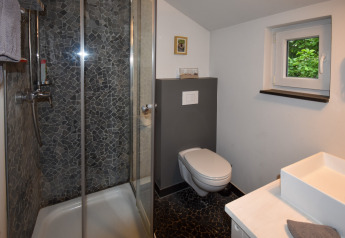 Salle de bains moderne dans mobil-home avec douche, WC suspendu, petite fenêtre et lavabo blanc.