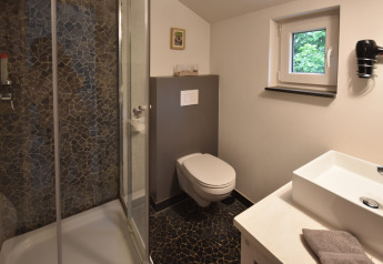 Modern bathroom in a mobile home featuring a shower, wall-mounted toilet, sink, and stone-tile flooring.