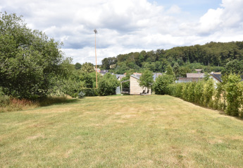 Large grassy yard with mobile home, trees, and hedges in Germany, viewed under a partly cloudy sky.