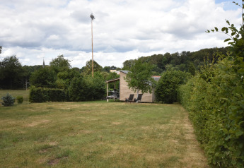Yard with mobile home Terra 2 Persons in Germany, green bushes and lounge chairs on the terrace.