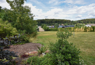 Vista su un grande giardino erboso con alberi, arbusti, case di villaggio e foresta nella campagna tedesca.