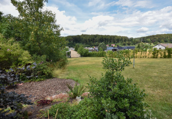 Vue sur un grand jardin verdoyant avec arbres, arbustes, maisons de village et forêt en Allemagne.