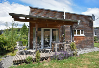Cabaña de madera con terraza y muebles de jardín en Holiday home «Magma 2 Persons», rodeada de vegetación en Alemania.