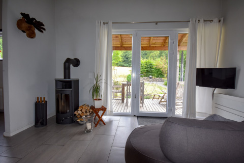 Woonkamer met houtkachel en grote ramen naar terras in vakantiehuis Magma, Duitsland.
