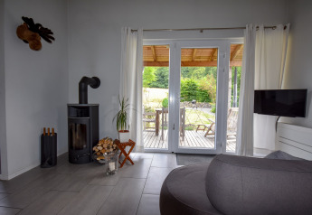 Salon avec poêle à bois et grandes fenêtres donnant sur la terrasse dans le gîte Magma, Allemagne.