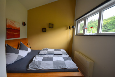 Modern bedroom with double bed, yellow accent wall and large windows at Holiday home Magma 2 Persons, Germany.