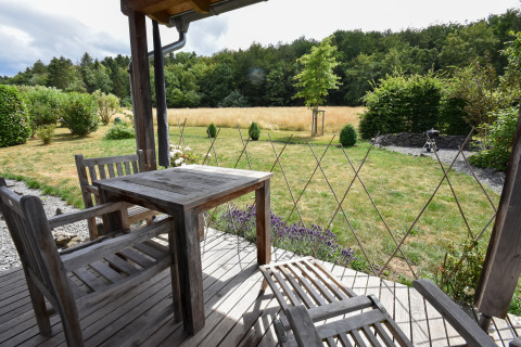 Terraza de madera con muebles de jardín y vistas a un prado y bosque en Holiday home Magma, Alemania.