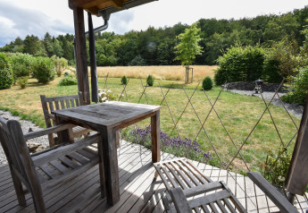 Houten terras met tuinmeubelen en uitzicht op grasveld en bos bij Holiday home Magma in Duitsland.