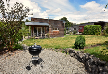 Havebillede af feriehus Magma 2 Persons i Tyskland, med grill og moderne træhuse i baggrunden.