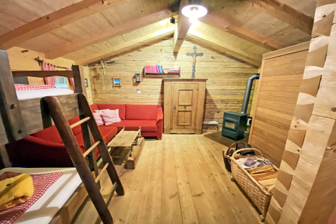 Gemütliches Chalet-Innenraum in der Almhütte mit Holzwänden, rotem Sofa, Stockbett und Holzofen.