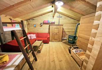 Cozy interior of Almhütte chalet featuring wood walls, red sofa, bunk bed, and a wood-burning stove.