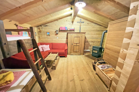 Gezellige inrichting van Almhütte-chalet met houten wanden, rood bankstel, stapelbed en houtkachel.