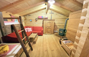 Cozy interior of Almhütte chalet featuring wood walls, red sofa, bunk bed, and a wood-burning stove.