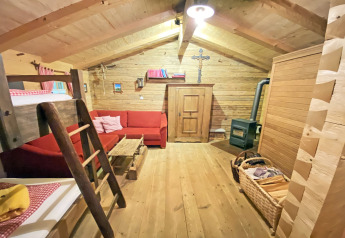 Cozy interior of Almhütte chalet featuring wood walls, red sofa, bunk bed, and a wood-burning stove.