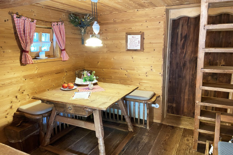 Gezellige eethoek in Almhütte-chalet met houten tafel, rood geruite gordijnen en authentieke sfeer.