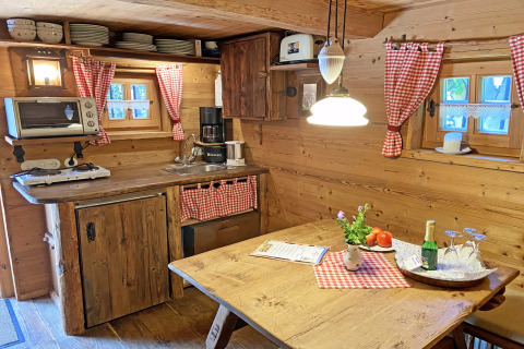 Gemütliche Chalet-Küche in der Almhütte mit Holzmöbeln, roten Karovorhängen und ländlichem Charme.