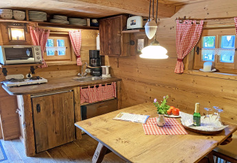 Cozy Almhütte chalet kitchen with wooden decor, checkered curtains, rustic table and warm lighting.