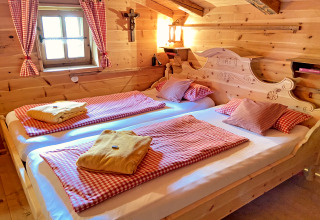 Gemütliches Schlafzimmer in einer Almhütte in Deutschland mit Holzwänden, zwei Betten und rotkarierten Decken.