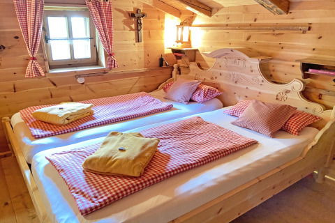 Gezellige houten slaapkamer in chalet Almhütte in Duitsland met twee bedden en rood geruite lakens.