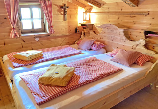 Gezellige houten slaapkamer in chalet Almhütte in Duitsland met twee bedden en rood geruite lakens.