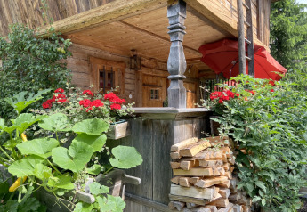 Accogliente chalet Almhütte in Germania con fiori rossi, ortaggi e legna accatastata all’esterno.