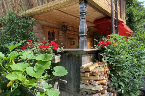 Gezellige Almhütte in Duitsland met rode bloemen, groenten en keurig gestapeld brandhout buiten.