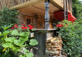 Charming Almhütte chalet in Germany with red flowers, vegetables, and stacked firewood outside.