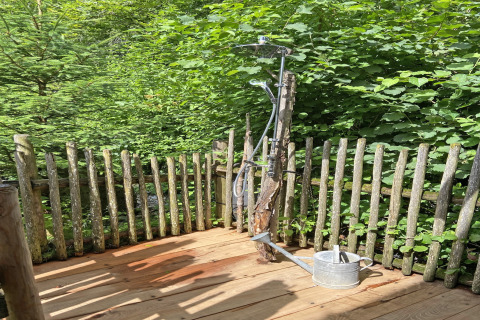 Buitendouche op een houten terras bij chalet Almhütte, omringd door groene natuur en een houten hek.