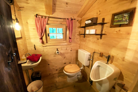Rustikales Badezimmer im Almhütte-Chalet mit Holzdekor, Fenster, WC, Urinal und roten Vorhängen.
