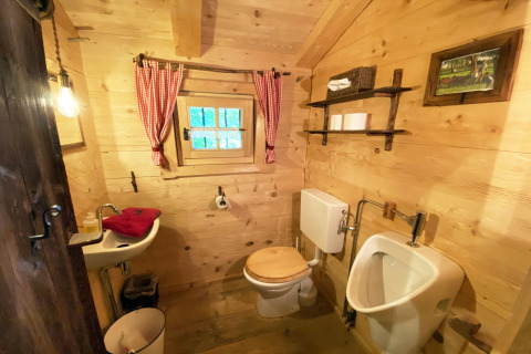 Rustieke badkamer in houten stijl bij chalet Almhütte, met toilet, urinoir en rode gordijnen.