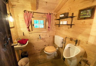 Rustieke houten badkamer in Almhütte-chalet met toilet, urinoir, klein wastafel en rode gordijnen.