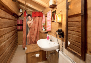 Frau an der Dusche in rustikalem Holzbad einer gemütlichen Almhütte in Deutschland, warm beleuchtet.