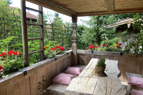 Rustieke houten tafel met rode bloemen en tuinuitzicht op de veranda van chalet Almhütte in Duitsland.
