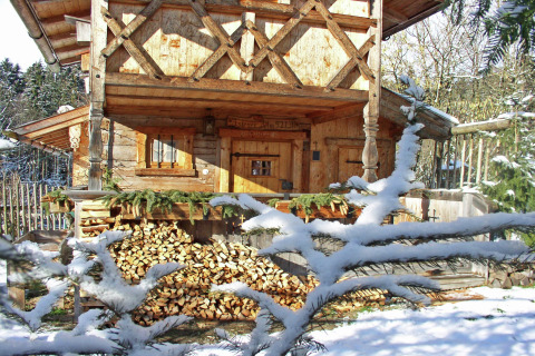 Met sneeuw bedekt houten chalet 'Almhütte' in Duitsland, met stapels haardhout en besneeuwde dennentakken.