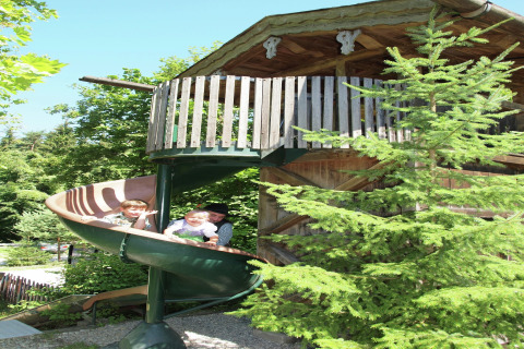 Twee kinderen en een volwassene glijden van een spiraalglijbaan bij chalet 