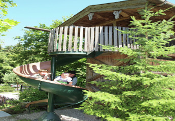 Two children and an adult play on a spiral slide at the chalet "Almhütte" in Germany, enjoying the sun.