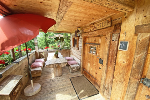 Houten veranda bij chalet 'Almhütte' in Duitsland met zitbank, tafel, rode bloemen en gezellige sfeer.
