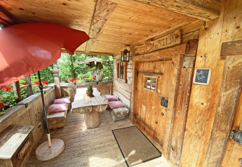 Wooden porch at chalet 'Almhütte' in Germany with bench, table, red flowers, and a cozy rustic atmosphere.