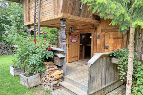 Rustieke ingang van chalet ‘Almhütte’ in Duitsland, omgeven door hout, bloemen en groen.