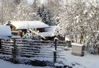 Paesaggio invernale innevato allo chalet Almhütte in Germania con baite in legno e alberi coperti di neve.