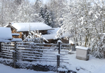 Snow-covered winter scene at Almhütte chalet in Germany with wooden huts and trees blanketed in snow.