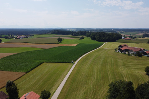 Landschapsfoto met groene velden, een weg en een Almhütte-chalet te midden van landbouwgrond.
